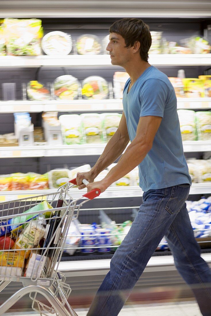 Junger Mann schiebt einen Einkaufswagen in einem Supermarkt