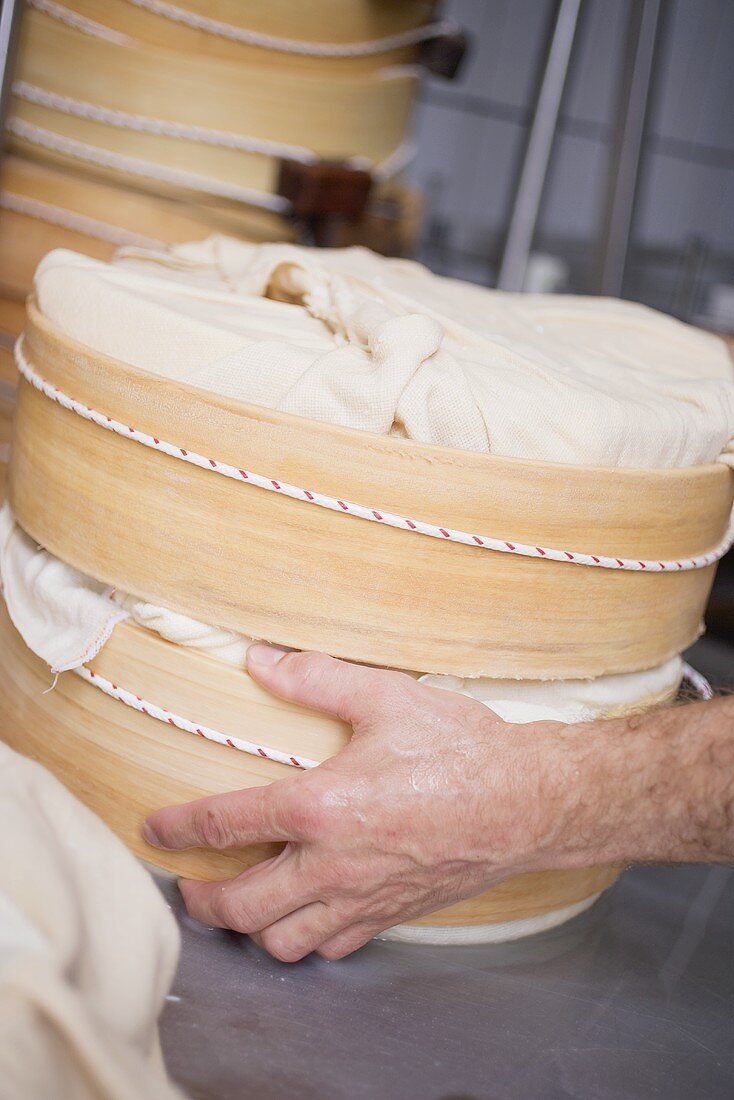 Hand hält runde Holzformen mit eingewickeltem Käse