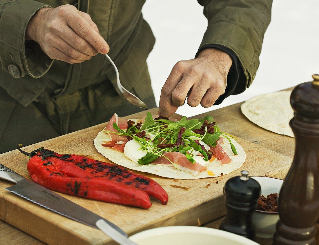 Topping a piadina with rocket and raw ham