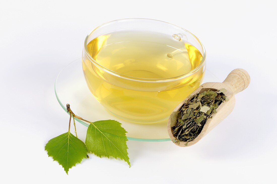 Birch leaf tea in glass cup, tea leaves in wooden scoop