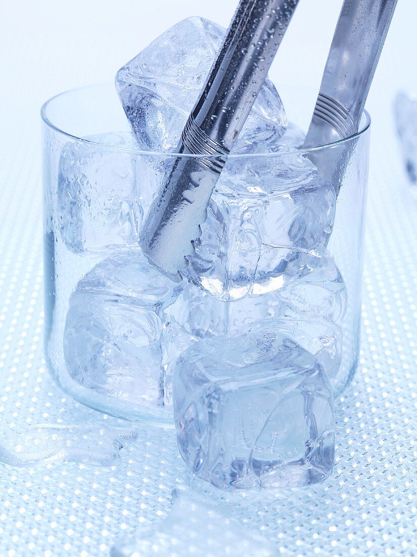 Several ice cubes in glass with ice tongs