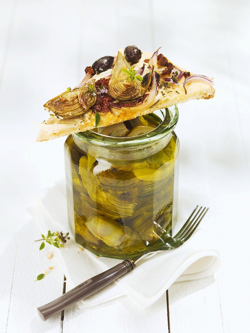 Slice of pizza on a jar of pickled artichokes