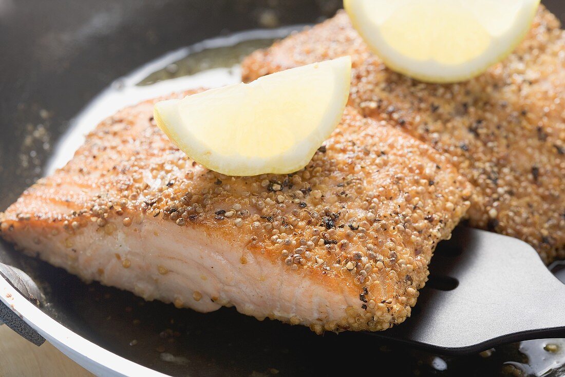 Fried salmon fillet with lemon wedges in frying pan