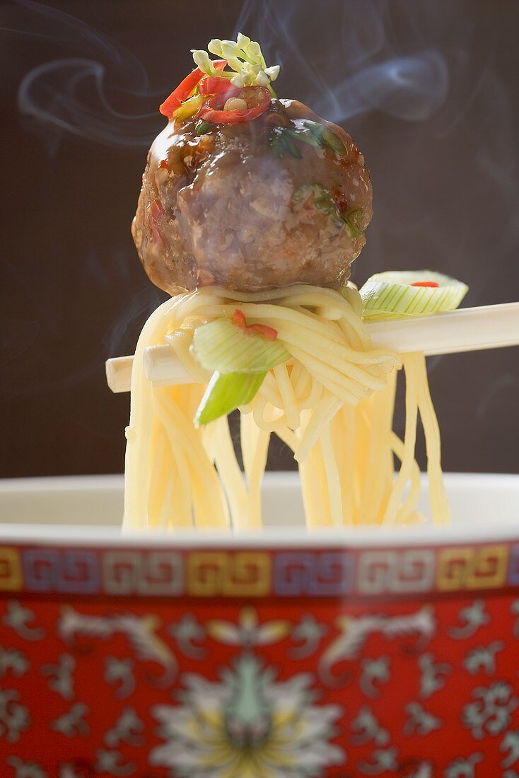 Egg noodles with spicy meatball on chopsticks (China)