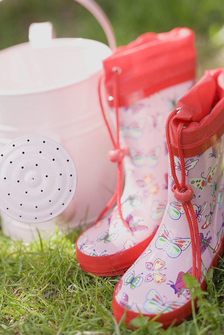 Gummistiefel und Giesskanne für Kinder auf der Wiese