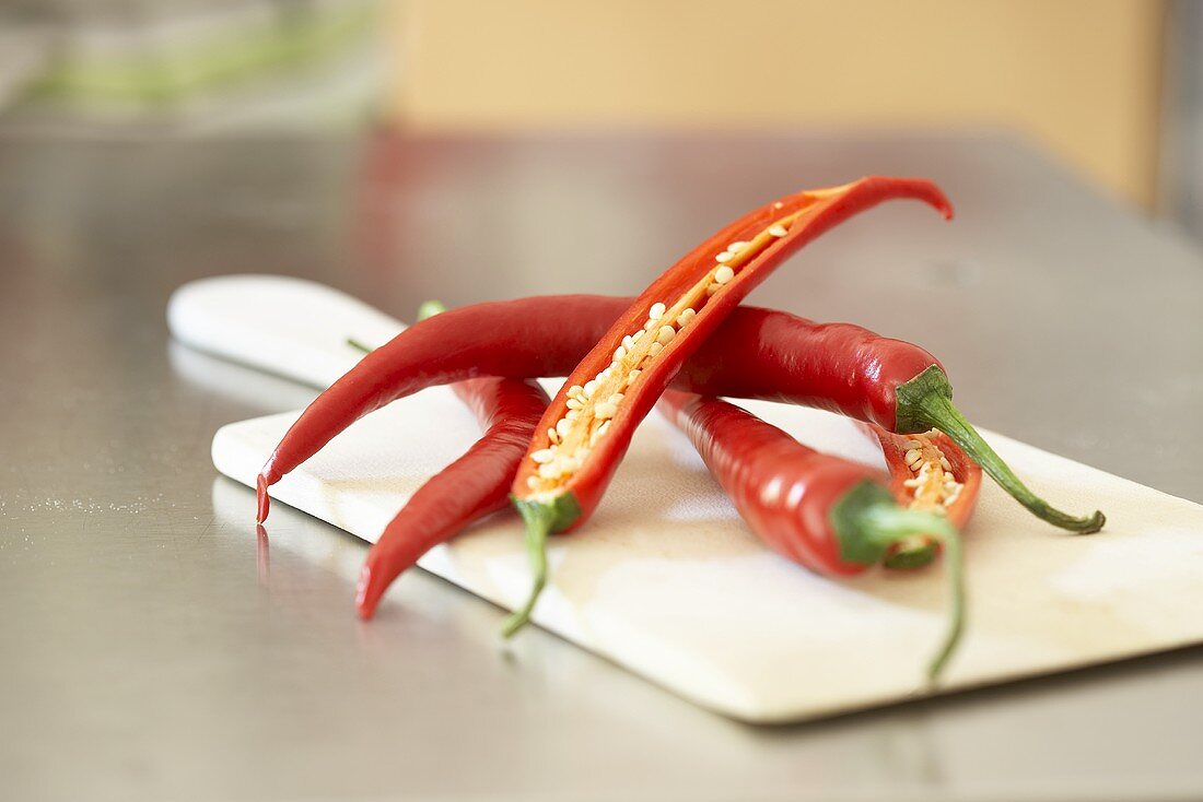 Red chillies, whole and halved, on chopping board