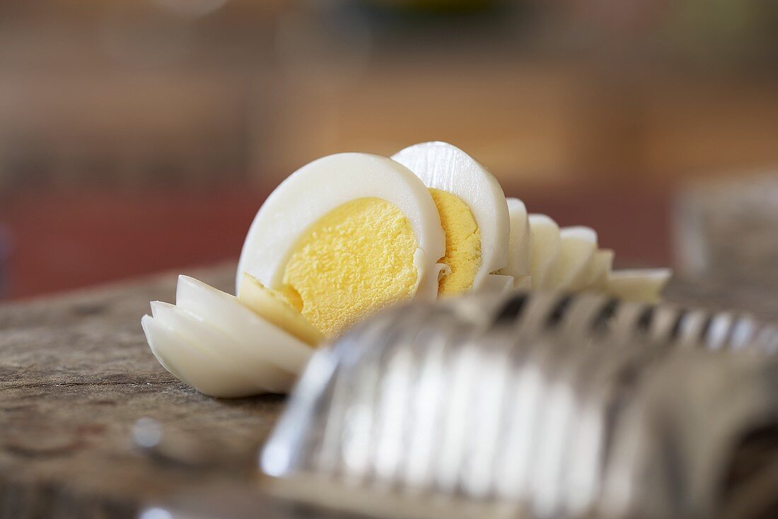 Gekochtes Ei, in Scheiben geschnitten, neben Eierschneider