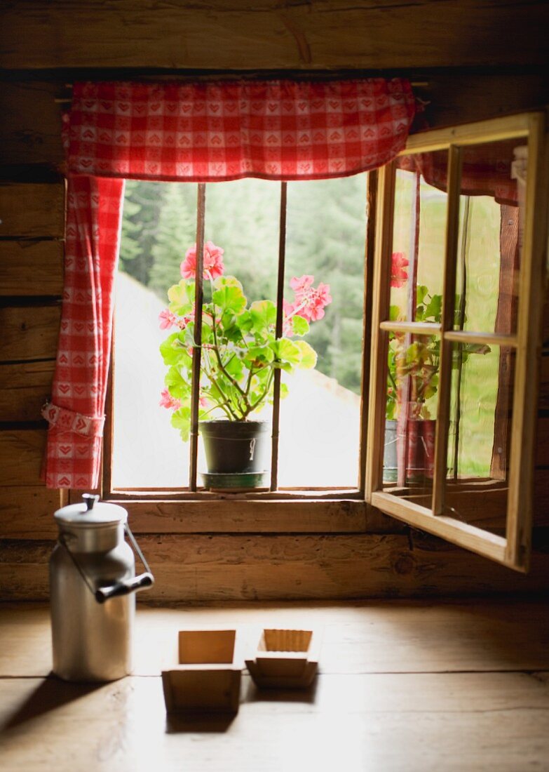 Milchkanne und Holzmodeln vor dem Fenster einer Almhütte