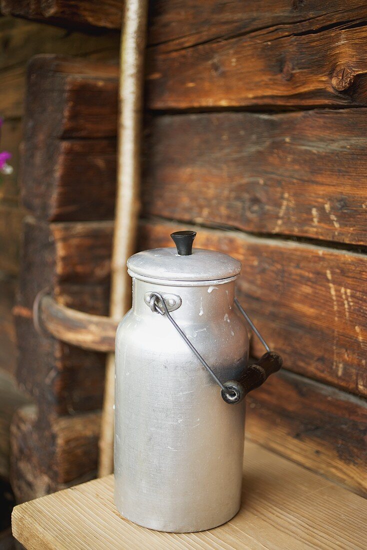 A close up of a milk can in front of wooden chalet