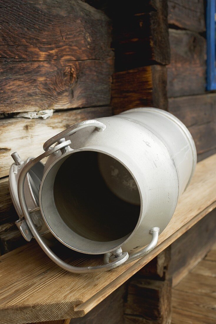 Empty milk can on wooden bench in front of Alpine chalet