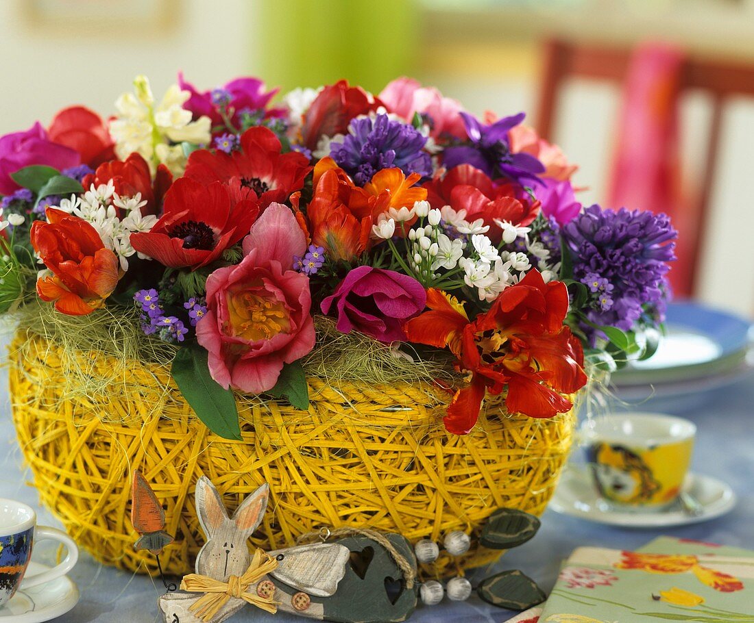 Ostergesteck mit Tulpen, Hyazinthen, Kronenanemone und Milchstern im Korb, Holz-Osterhase liegend