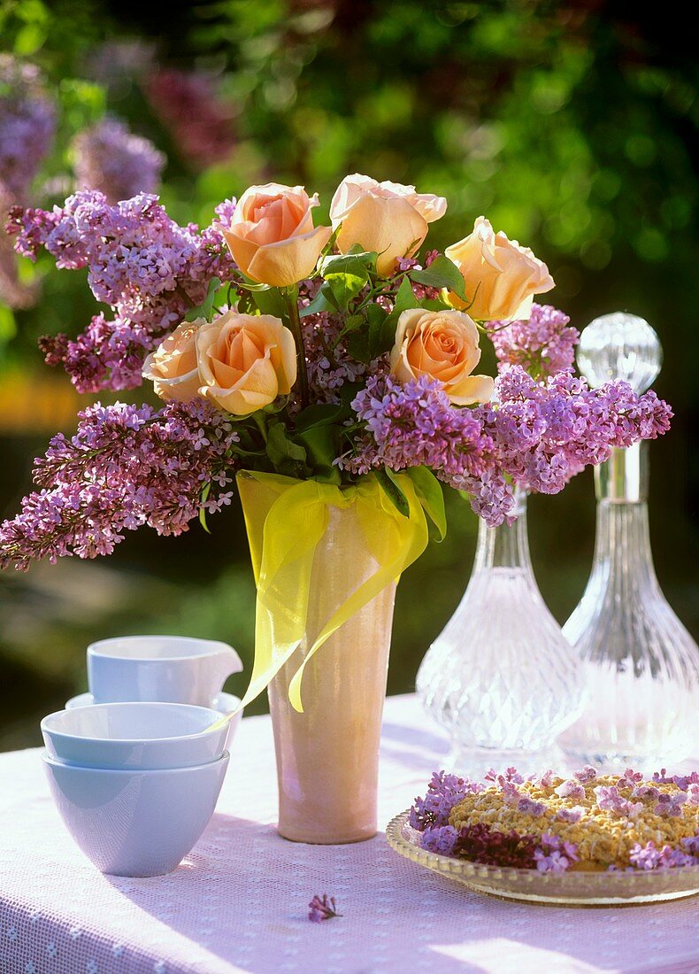 Crumble cake & vase of roses & lilac on table out of doors