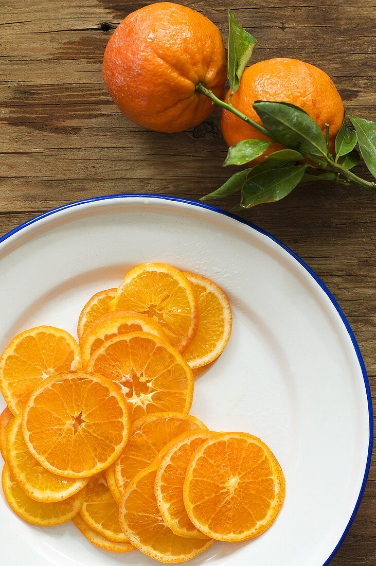 Plate of orange slices and oranges with leaves
