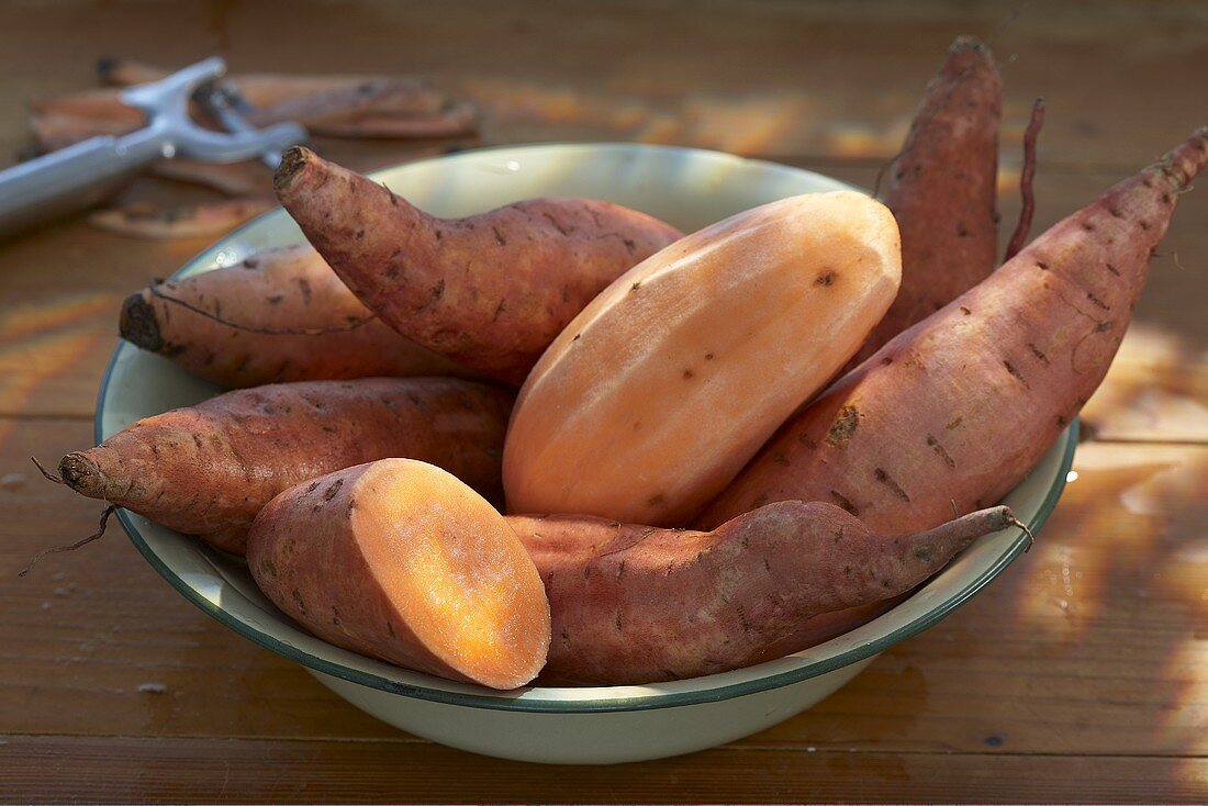 Sweet potatoes in a bowl, whole, halved and peeled