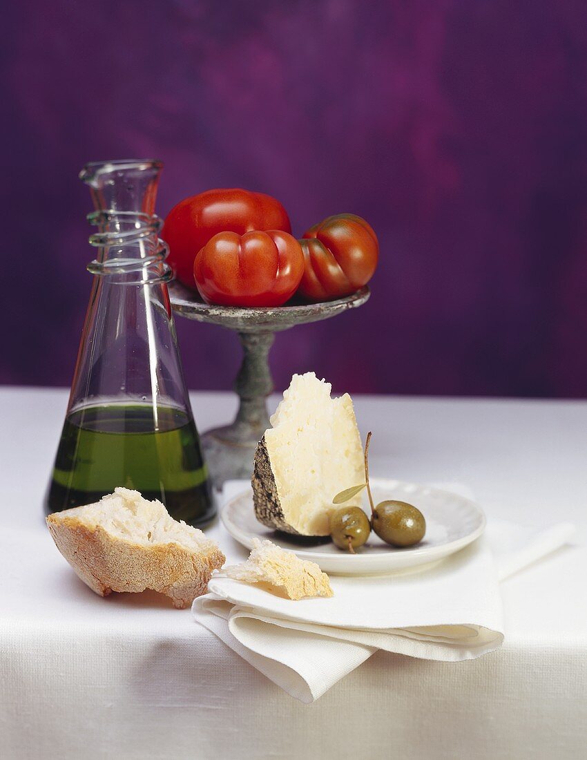 Stillleben mit Weißbrot, Parmesan, Oliven, Olivenöl & Tomaten