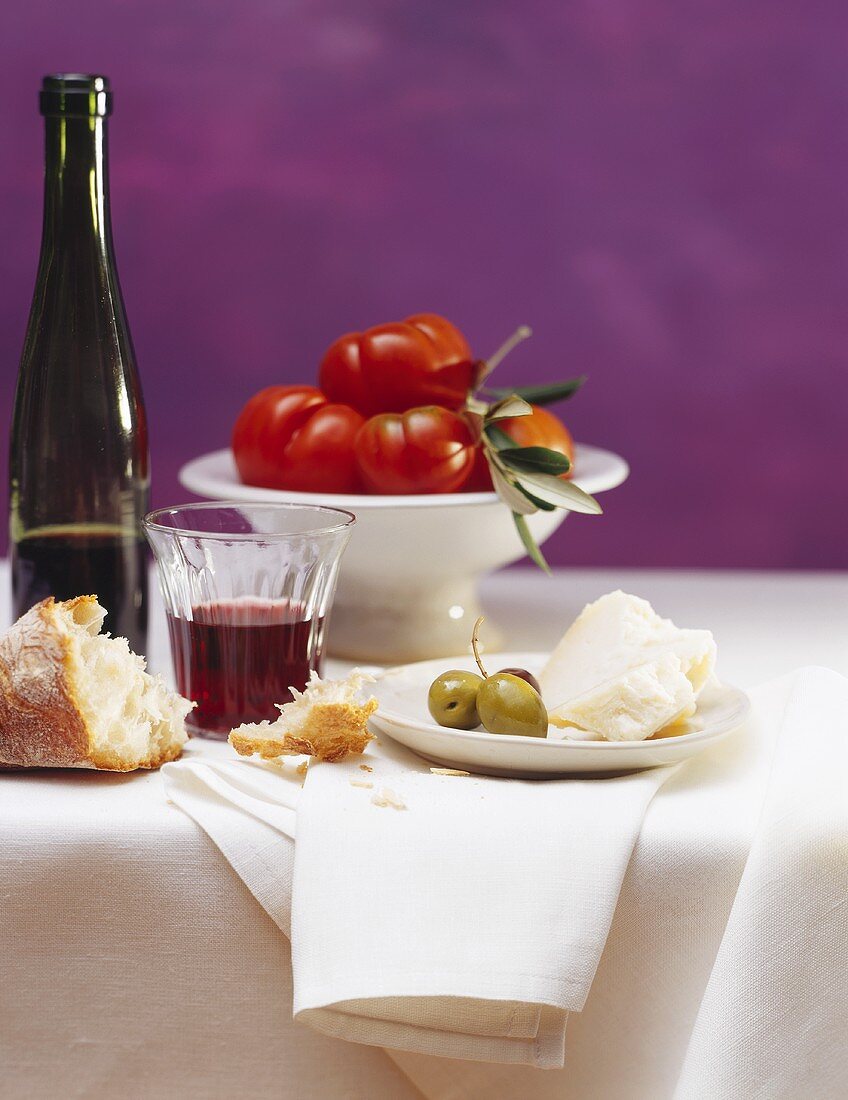 Stillleben mit Weißbrot, Parmesan, Oliven, Rotwein & Tomaten