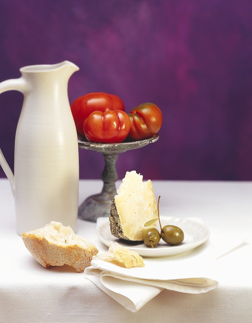 Stillleben mit Weißbrot, Parmesan, Oliven, Weinkrug & Tomaten