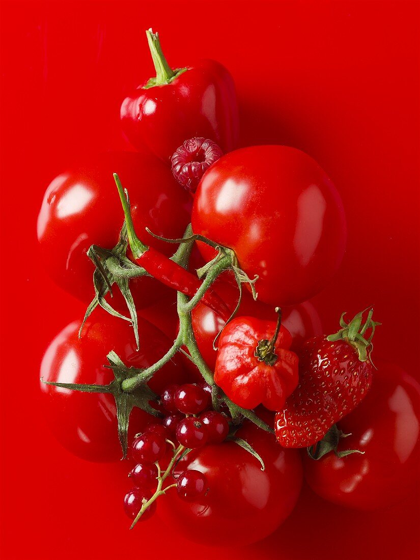 Red berries, tomatoes and chillies against red background