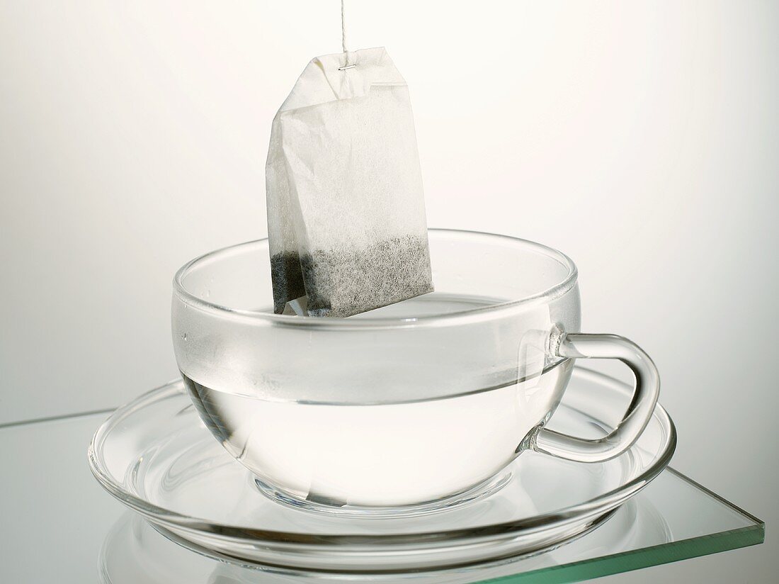 Teebeutel hängt über Glastasse mit heißem Wasser