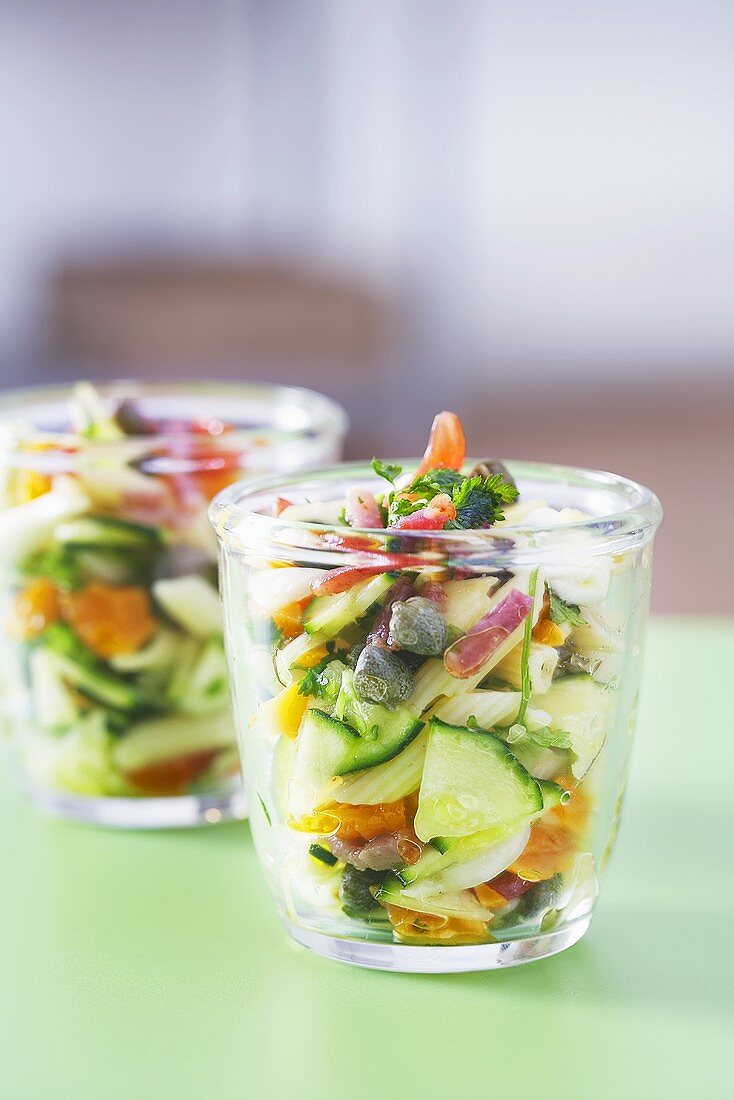 Mediteraner Nudelsalat mit Gemüse und Speck in zwei Gläsern