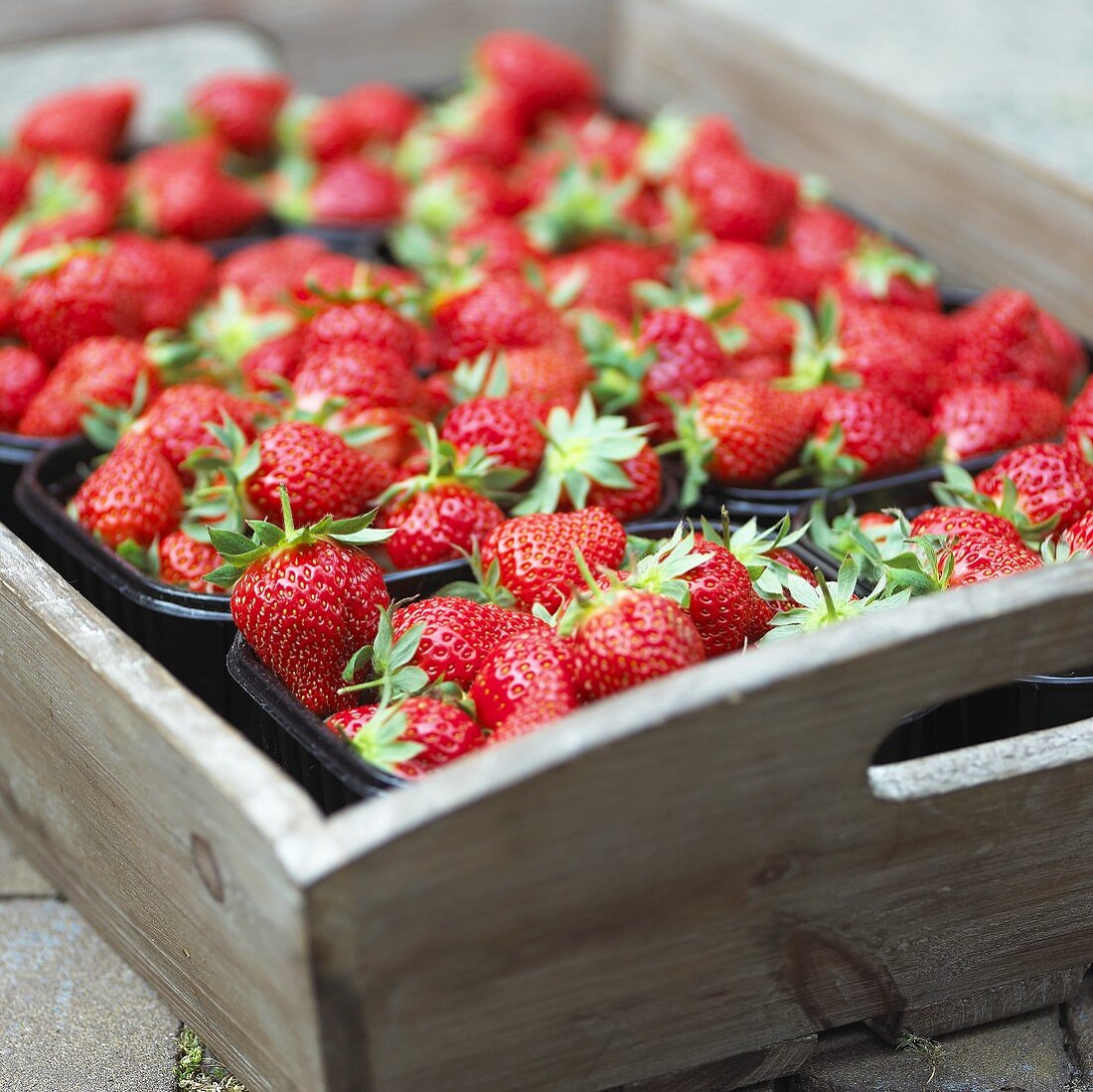 Strawberries in plastic punnets on wooden tray