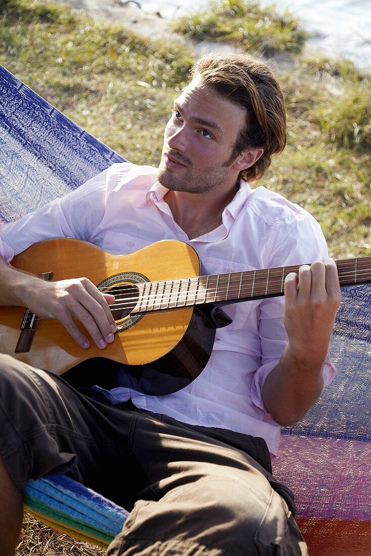 Young man sitting in a hammock playing a guitar