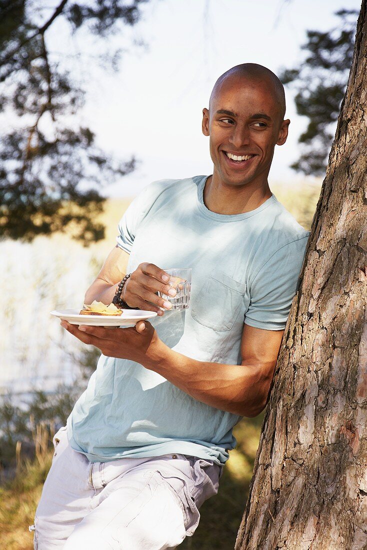 Young man standing by tree with crostini and glass of water