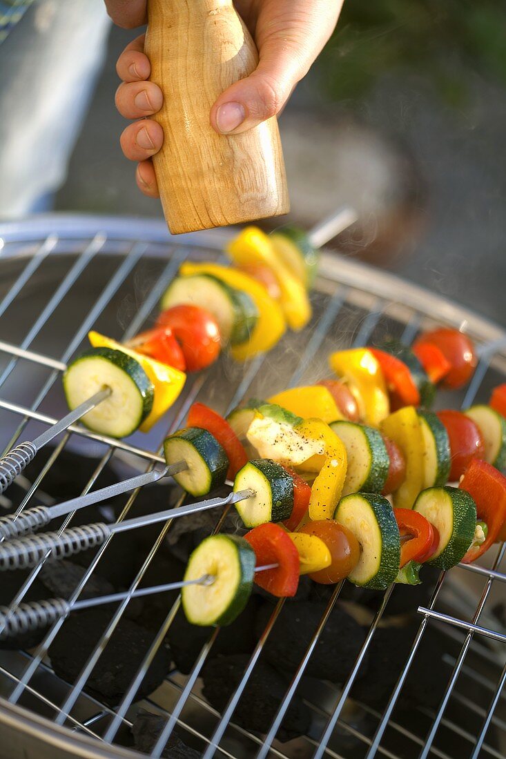 Vegetable skewers being seasoned on barbecue