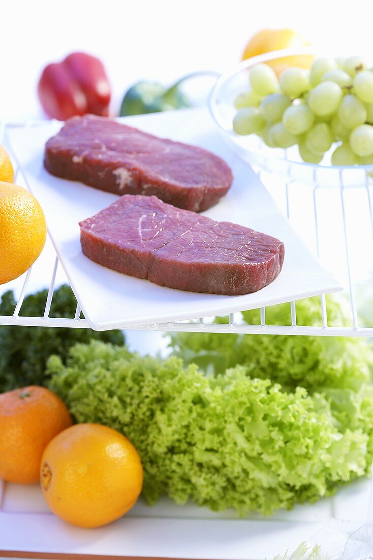 Beef steaks, salad and fruit in refrigerator