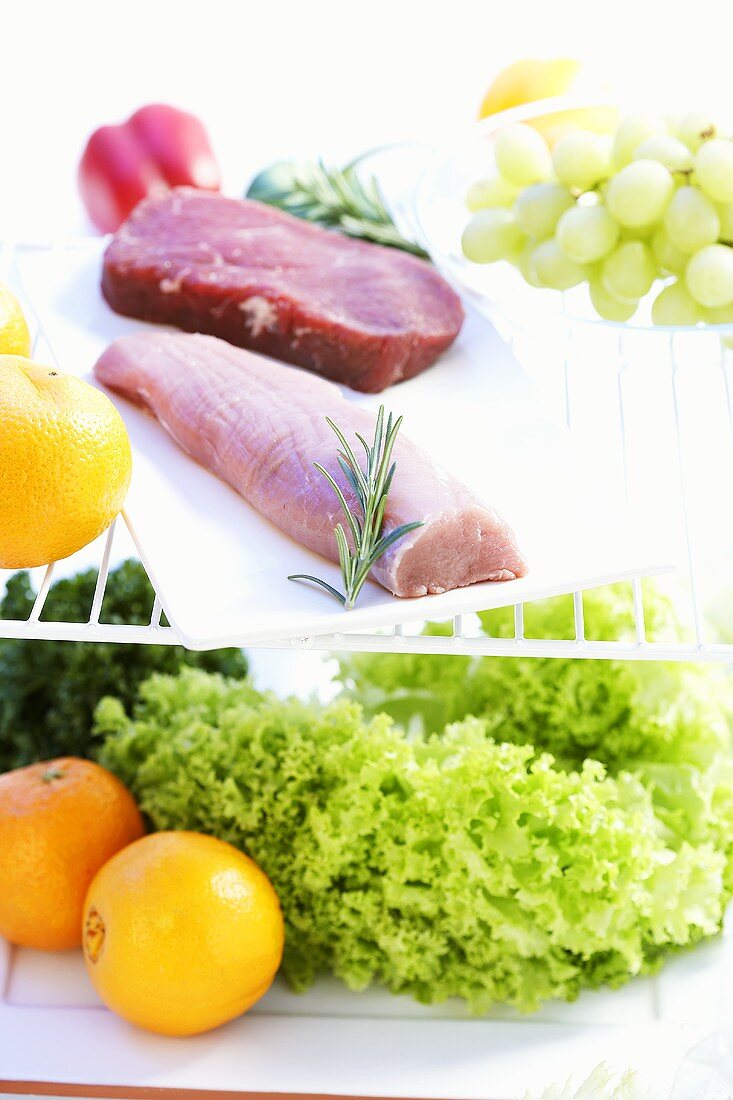 Pork fillet, beef steak, lettuce and fruit in refrigerator