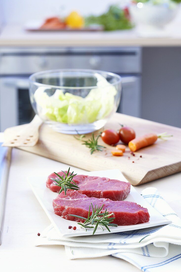Beef steaks and salad ingredients on a kitchen table