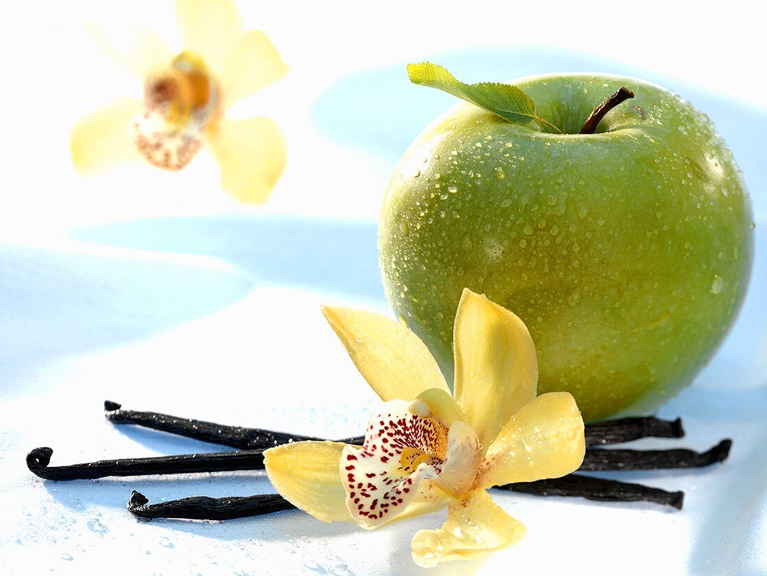 A Granny Smith apple with vanilla pods and orchid