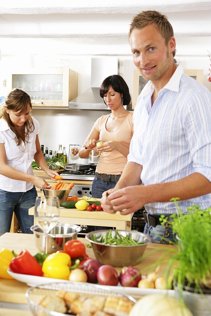 Drei junge Leute beim Gemüseputzen in der Küche
