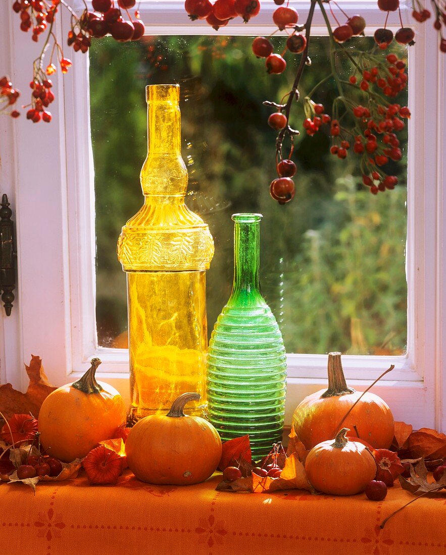 Pumpkins, coloured bottles & rose hip branches at window