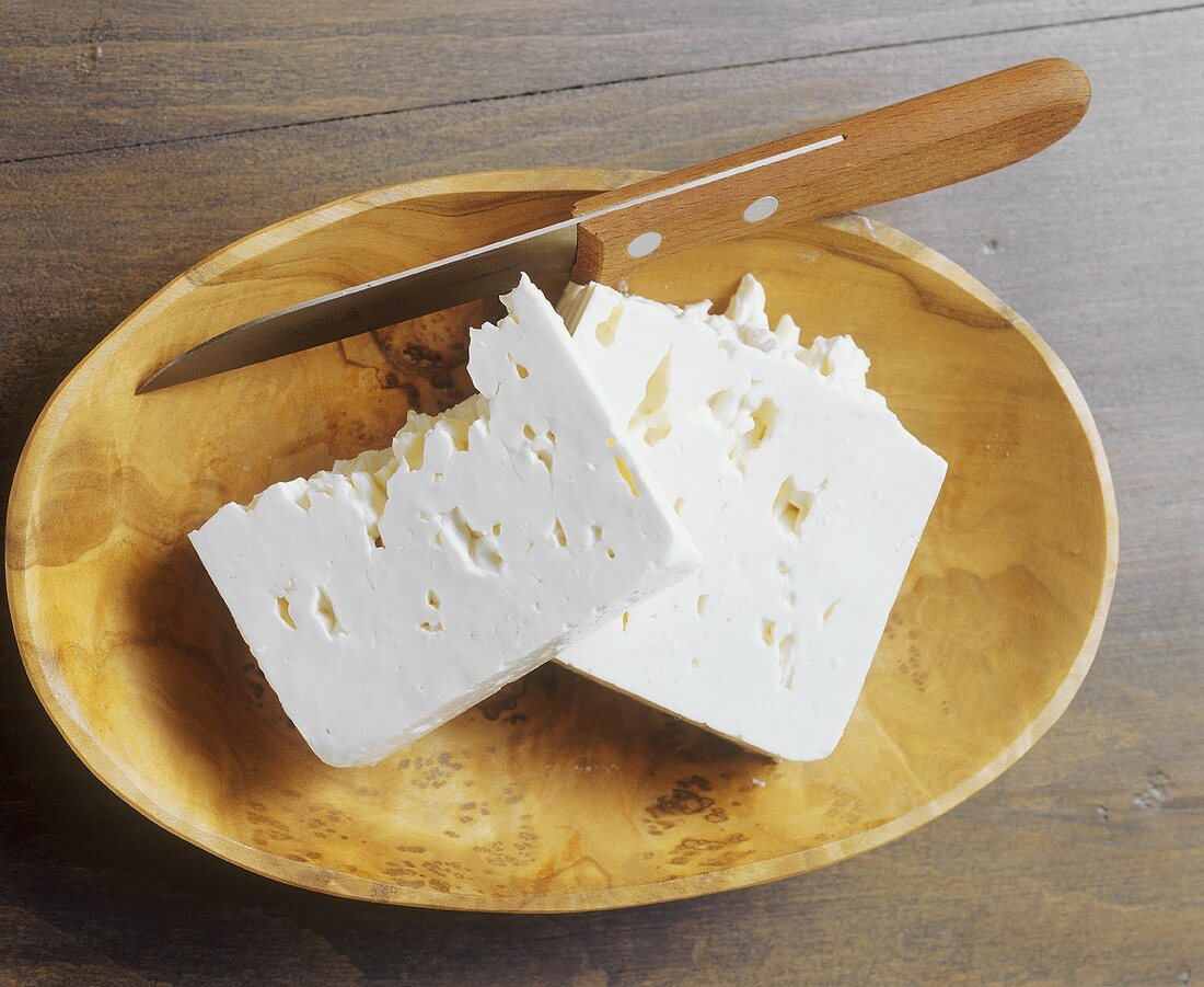 Feta with knife in a wooden bowl