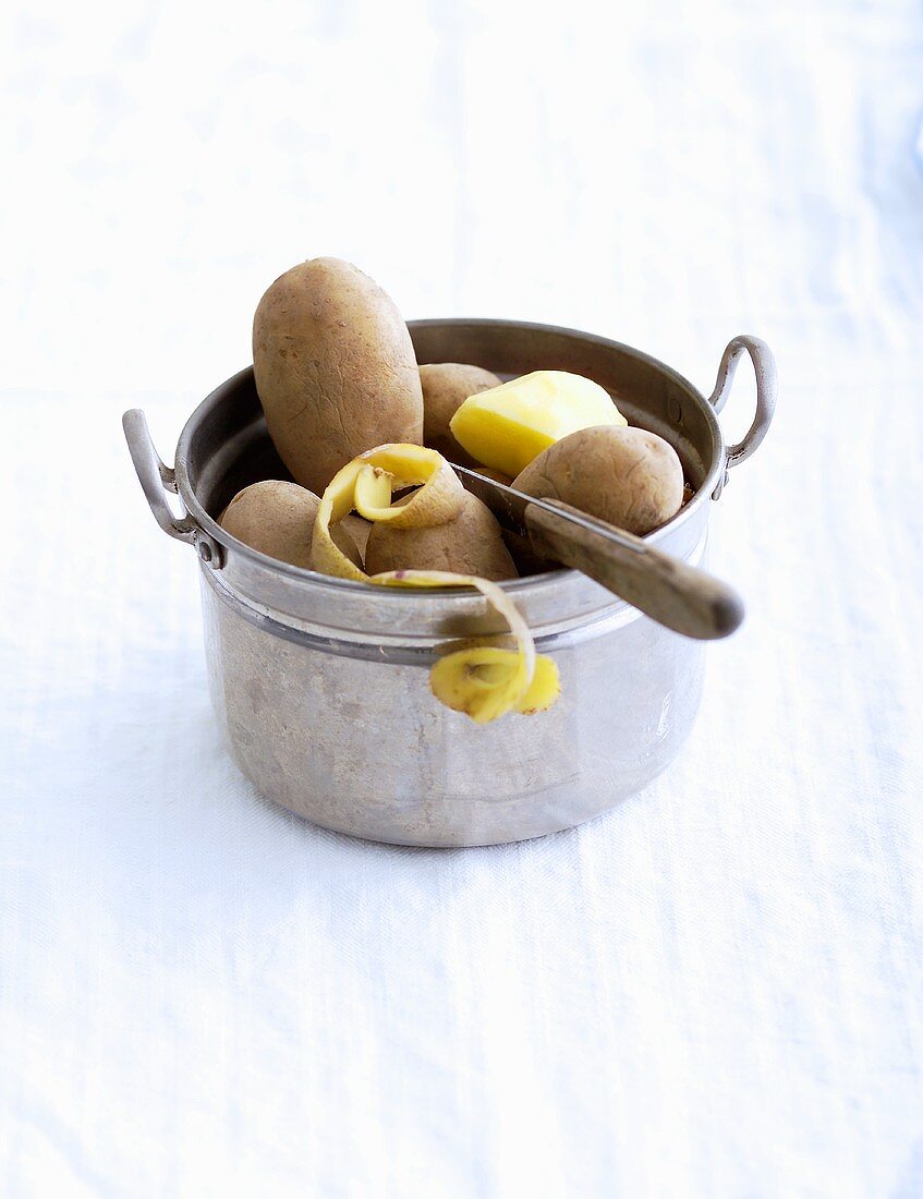 Unpeeled and peeled potatoes with knife in pot