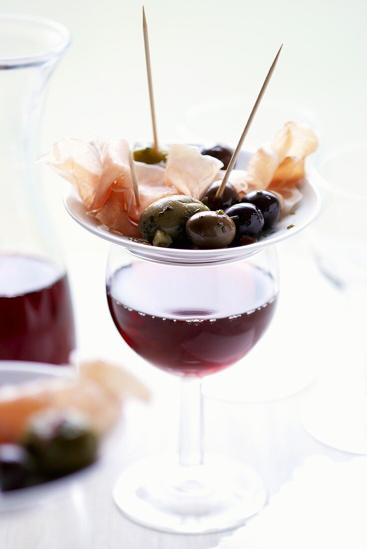 Plate of tapas: olives & Serrano ham on glass of red wine