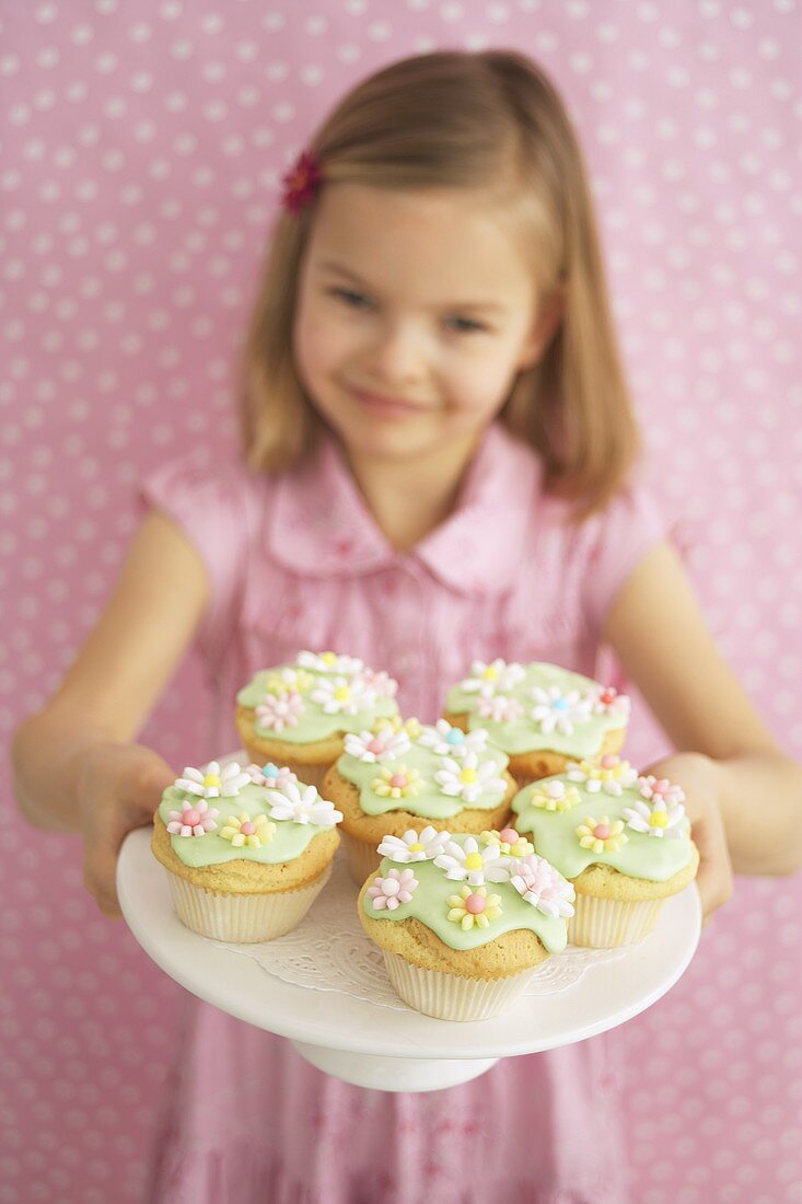 Mädchen hält Tablett mit verzierten Muffins