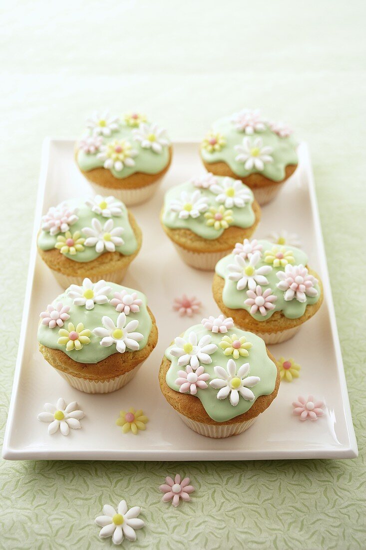 Muffins with green icing and sugar flowers on tray