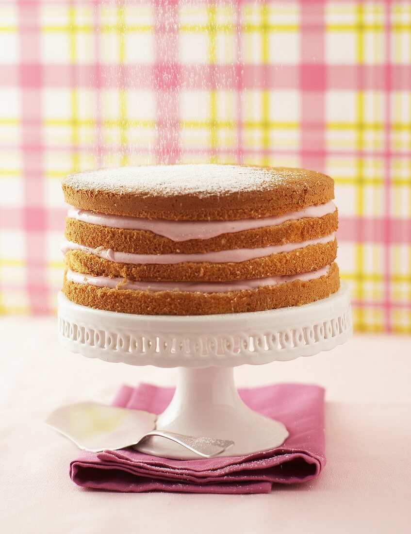 Dusting layered raspberry cream cake with icing sugar