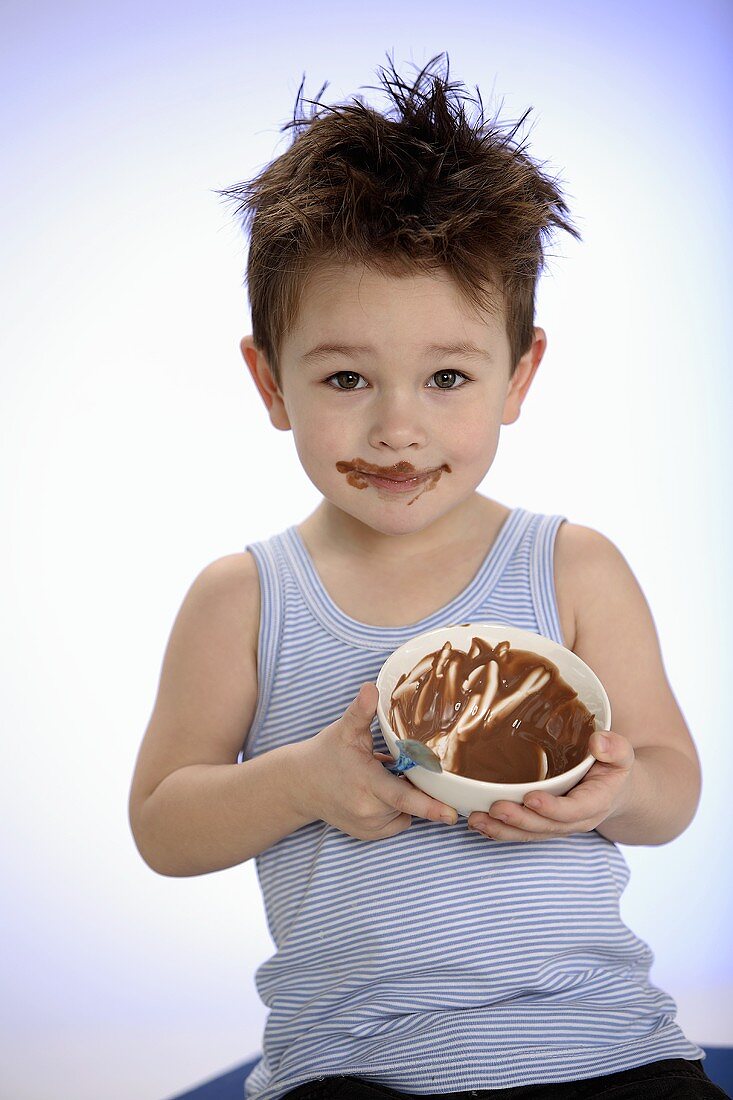 Small boy holding bowl of chocolate pudding towards camera