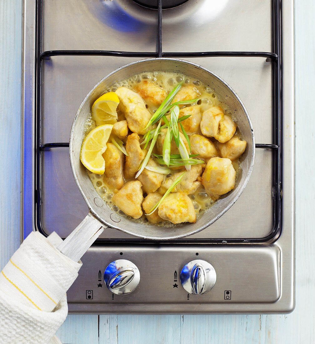 Lemon chicken in pan on gas cooker (overhead view)