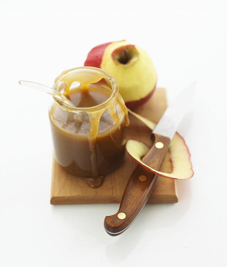 Apple caramel sauce in a jar and a peeled apple on a chopping board