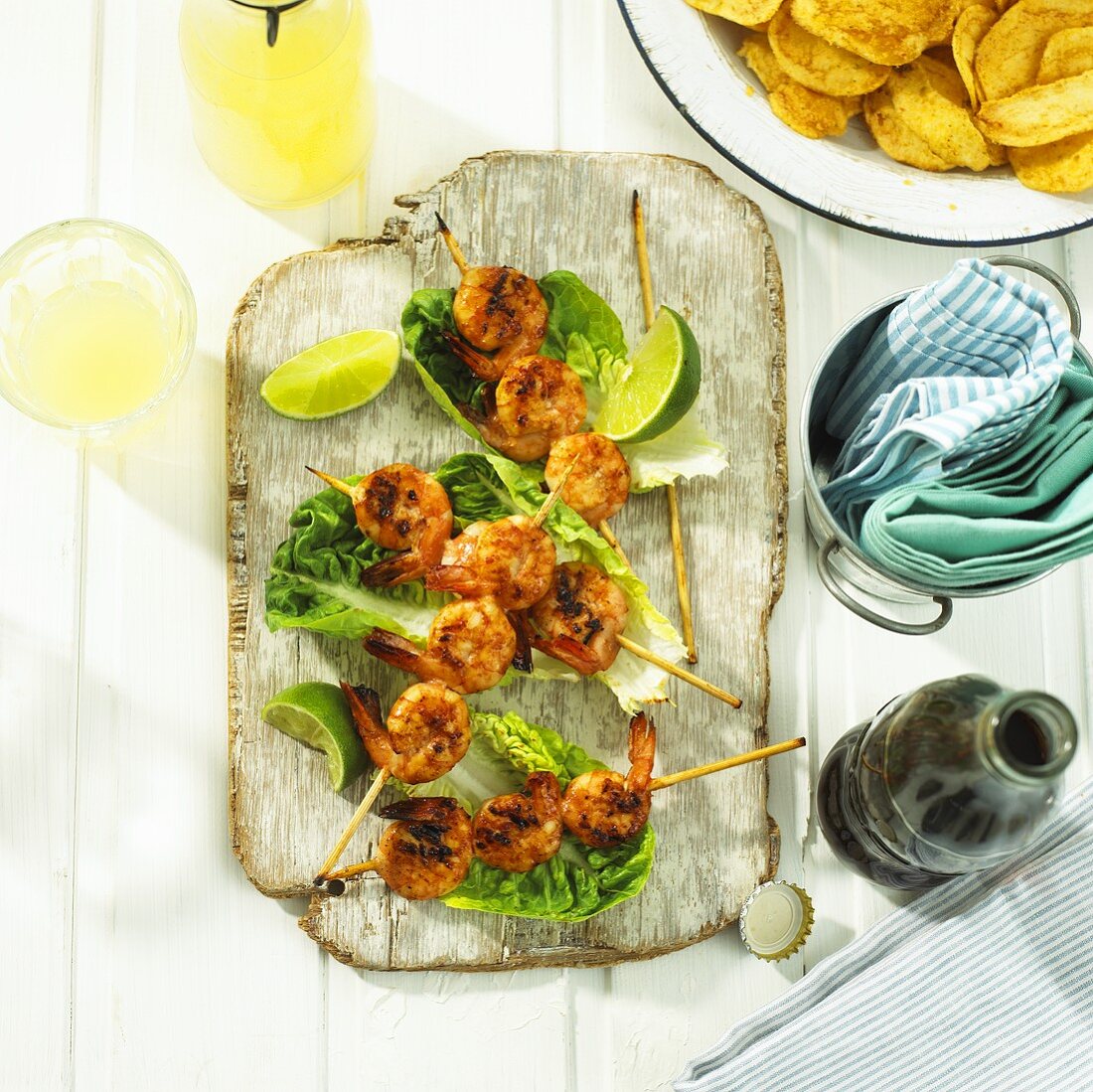 Prawn skewers on lettuce leaves, drinks, crisps