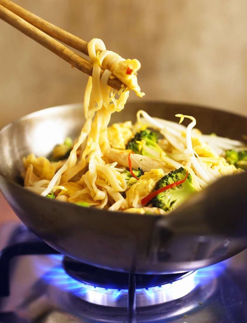 Noodles with chicken in wok on gas cooker