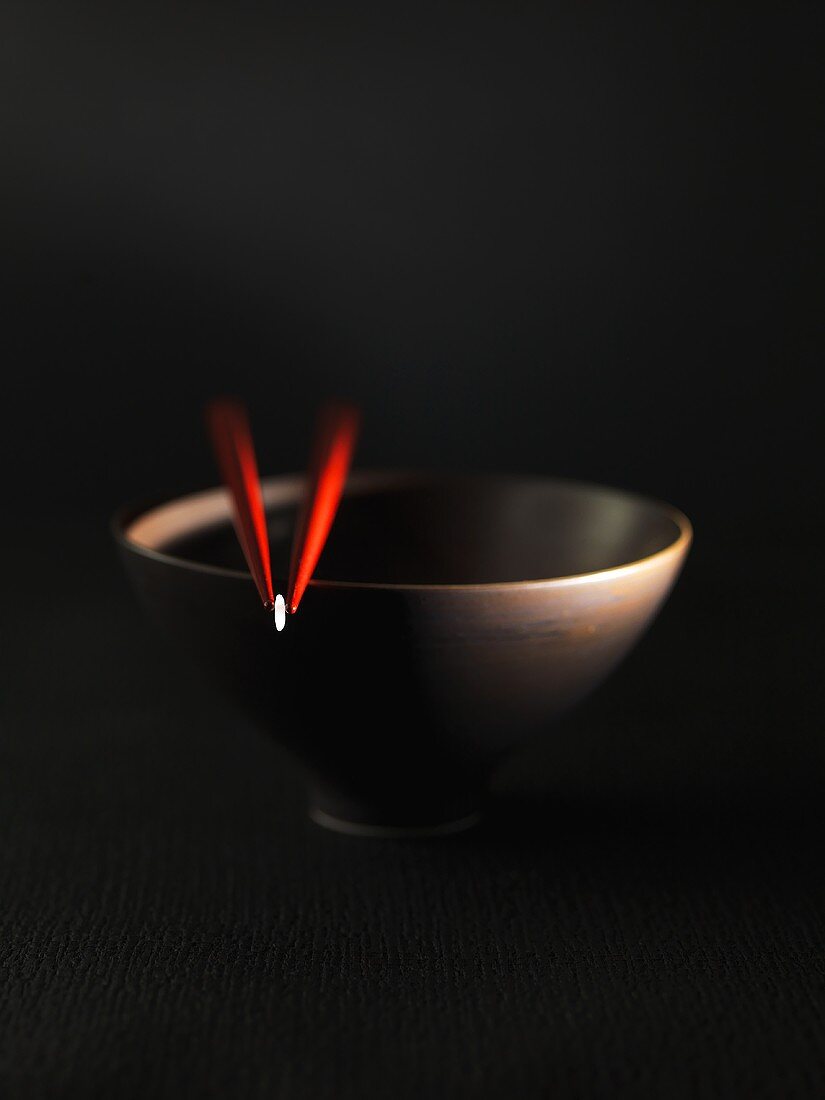 Grain of rice between red chopsticks on bowl