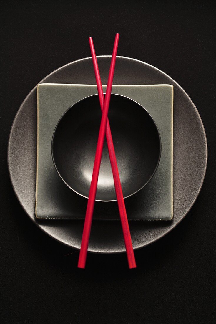 Black plates and bowl and red chopsticks (overhead view)