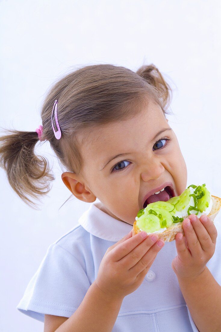 Kleines Mädchen isst Brot mit Gurken, Quark und Schnittlauch