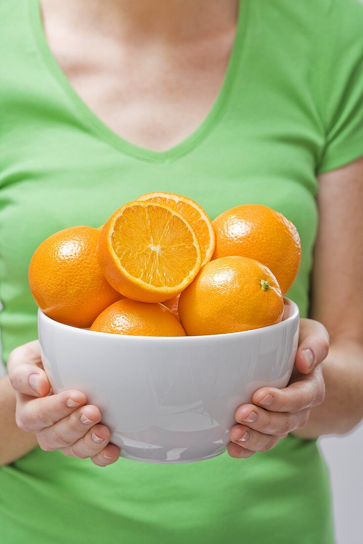 Woman holding bowl of fresh oranges