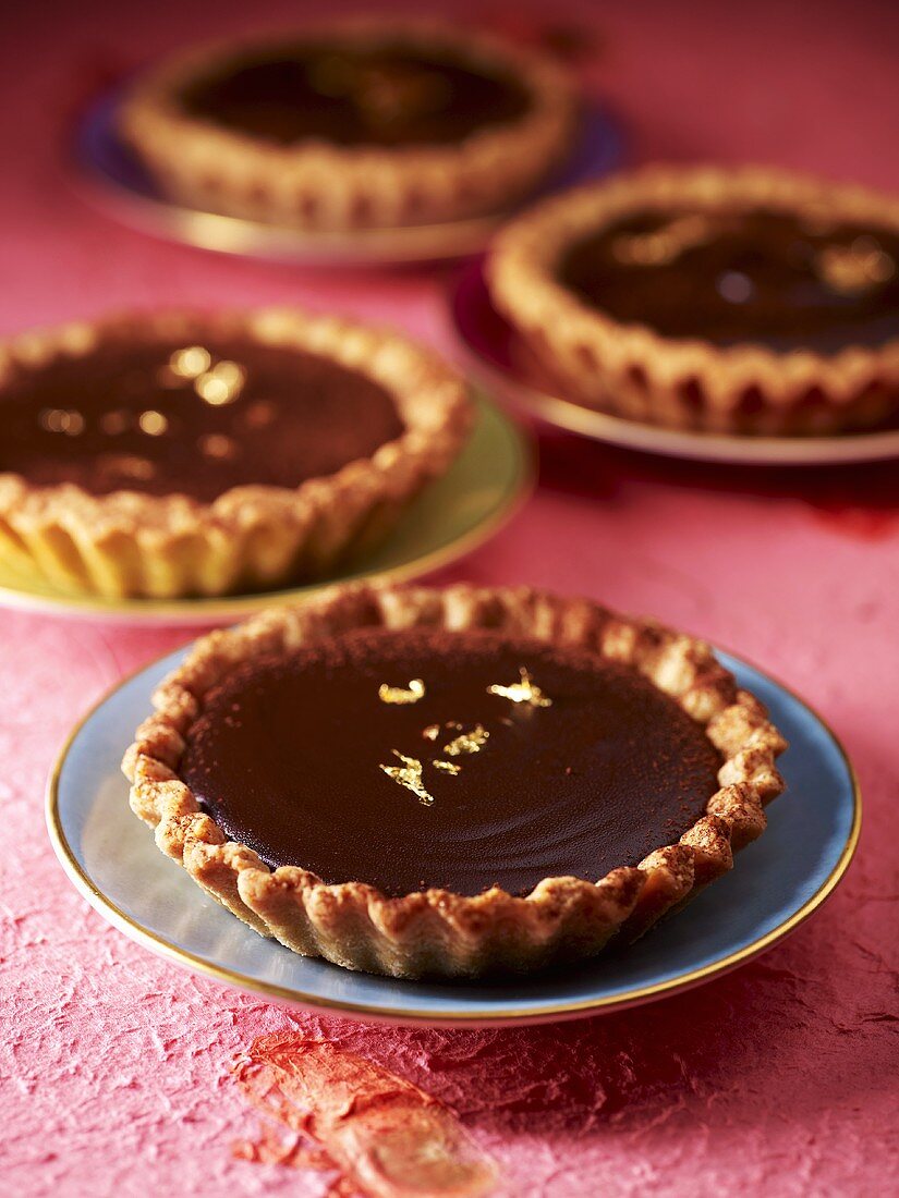 Small chocolate tarts with gold leaf on gold-rimmed saucers